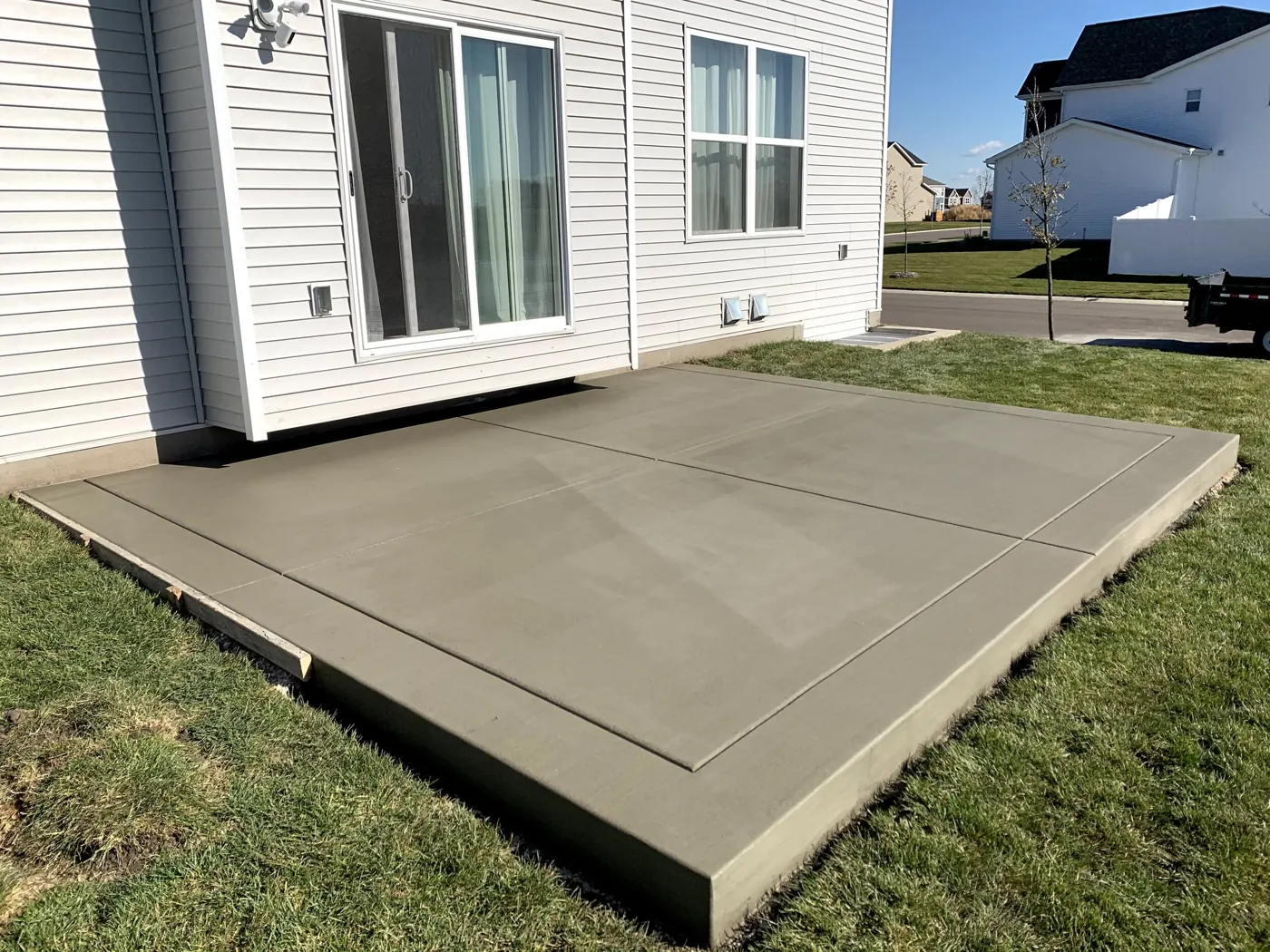Freshly poured plain concrete patio with tooled control joints behind a house